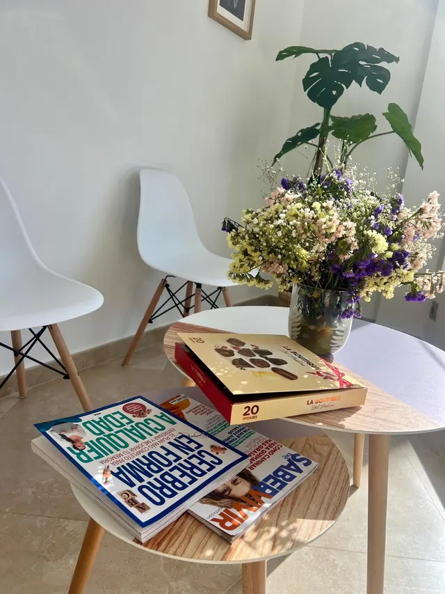 Detalle de la sala de espera: mesas de madera con revistas de salud, un ramo de flores secas y una planta